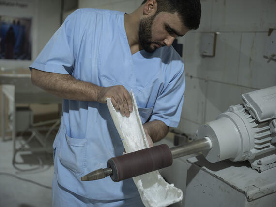 A man works on a machine shaping a plastic like material into a foot like structure 