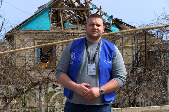 A humanitarian worker stands in front of a house destroyed in Ukraine's ongoing war.