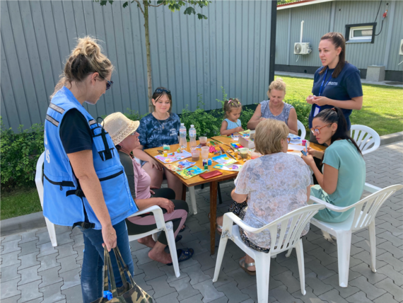 Hilary Stauffer (left), Head of OCHA Ukraine’s Kyiv Hub, speaks with residents of a modular town in Irpin, while a psychologist from International Medical Corps conducts a mental health and psychosocial support session with art therapy for seniors and children.