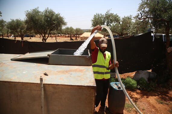 An aid workers fills a tank with water in Al-Hamra camp in Syria's Idleb governorate.