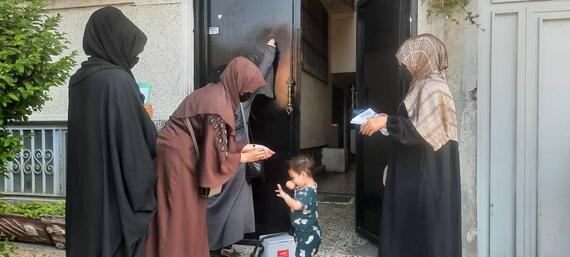 Three women administer polio drops to a small child at the entrance of a building in Kabul Province, Afghanistan, as part of a polio eradication campaign.