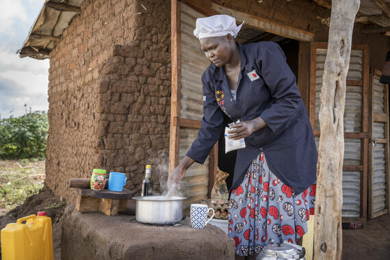 A South Sudanese woman wearing stirs a pot while preparing a meal outside her restaurant in a refugee settlement.